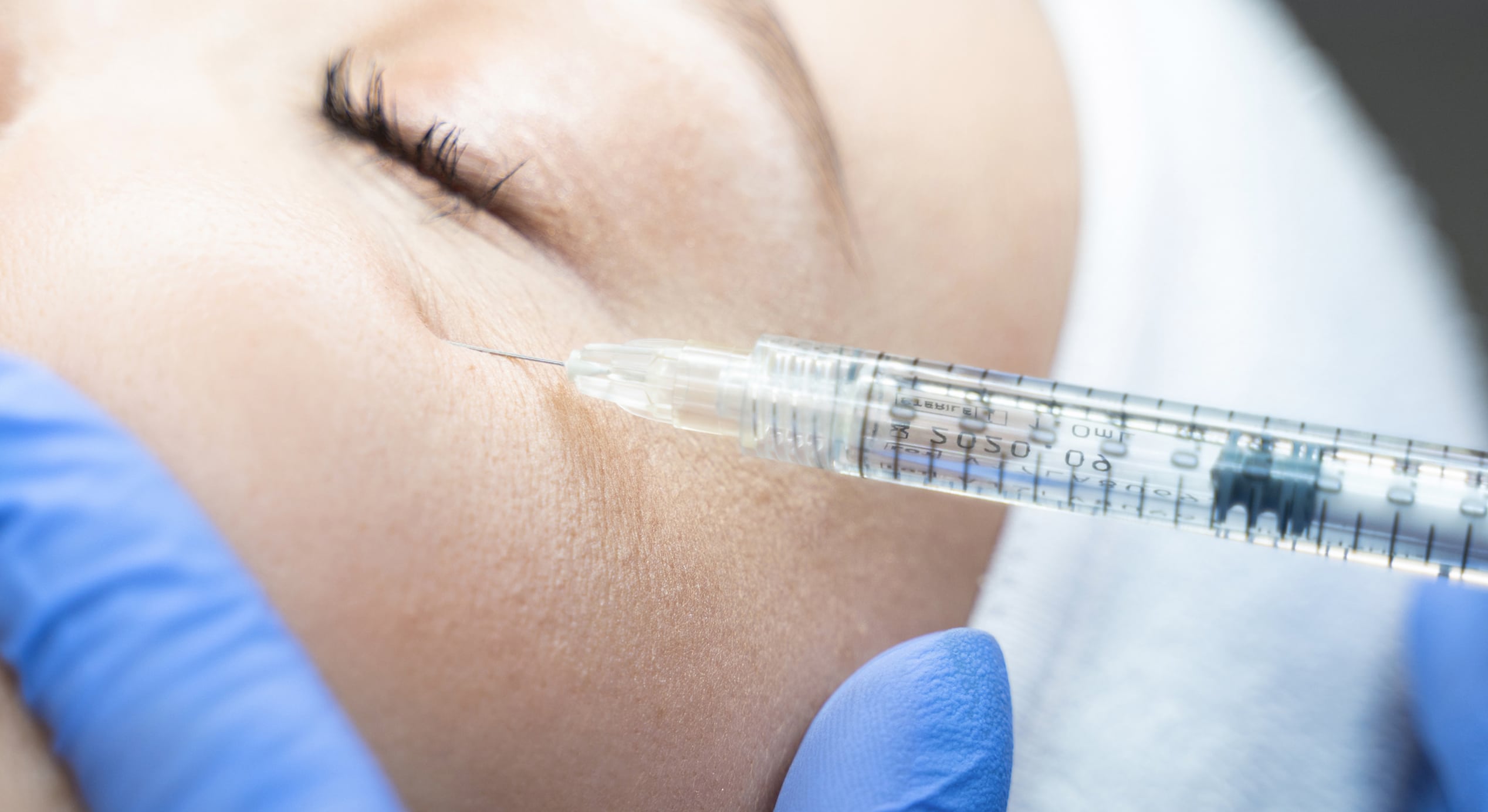 Close up woman being injected dermal filler into eye area by cosmetician 1