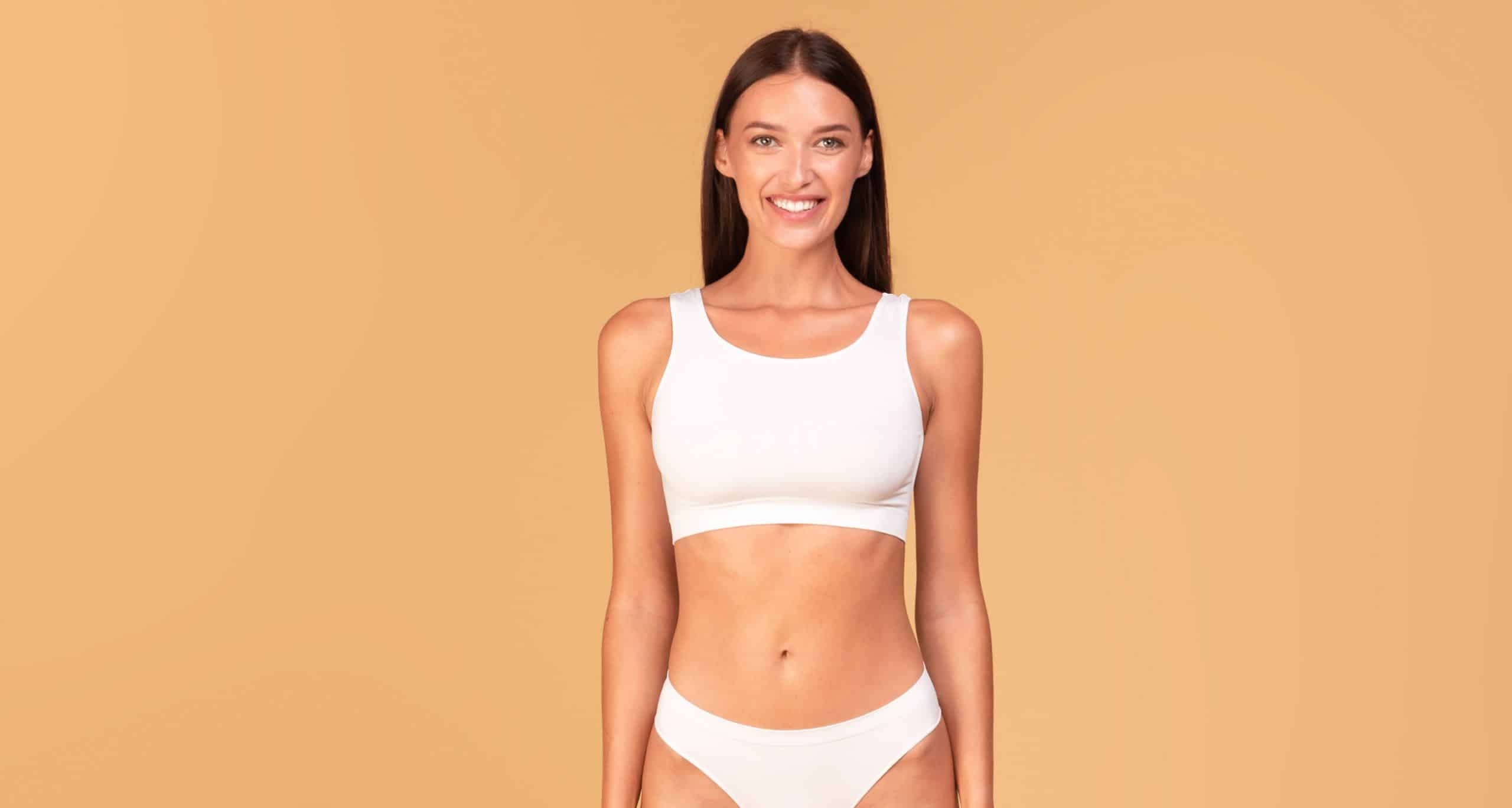 Full length frontal view slim woman with perfect body shape flat tummy posing beige studio background 2