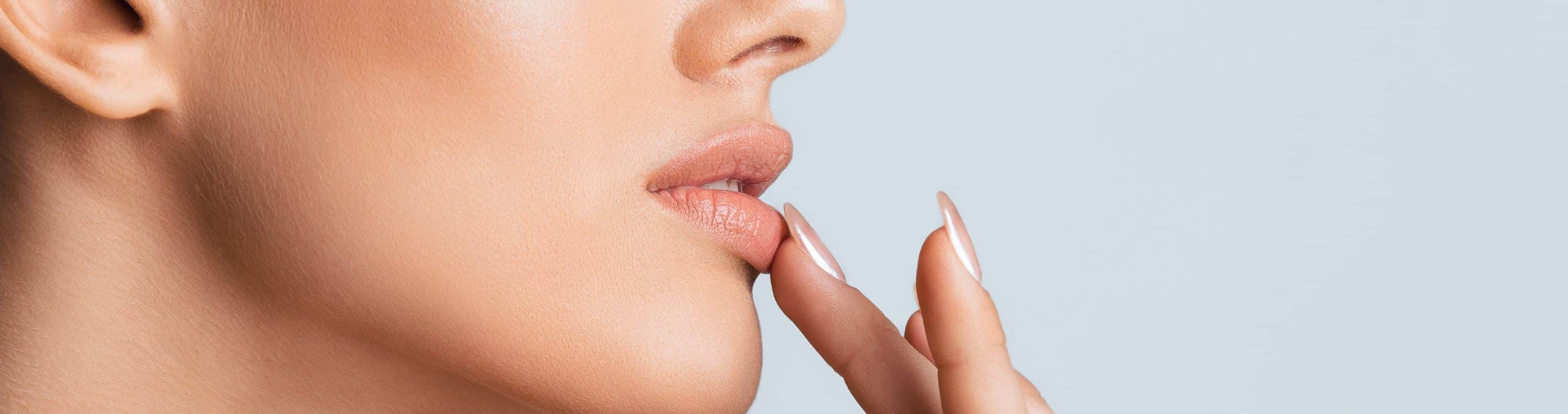Woman with light skin is captured profile her left hand gently touching her lower lip with her 1
